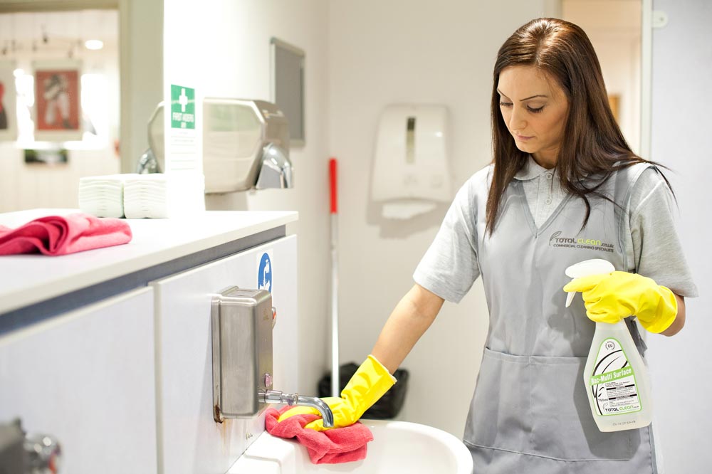 woman cleaning the sink of a medical facility with rubber yellow gloves and a spray bottle
