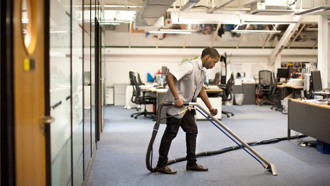 Man cleaning a hard floor surface in an office environment with a commercial hoover