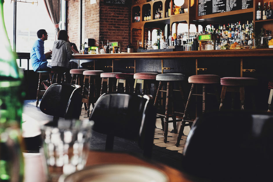 bar with seats the the front and a man and woman sitting on the end of the bar enjoying a drink