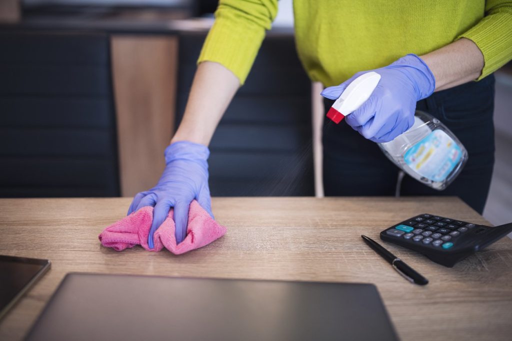 Woman with protective gloves cleaning workplace in office.